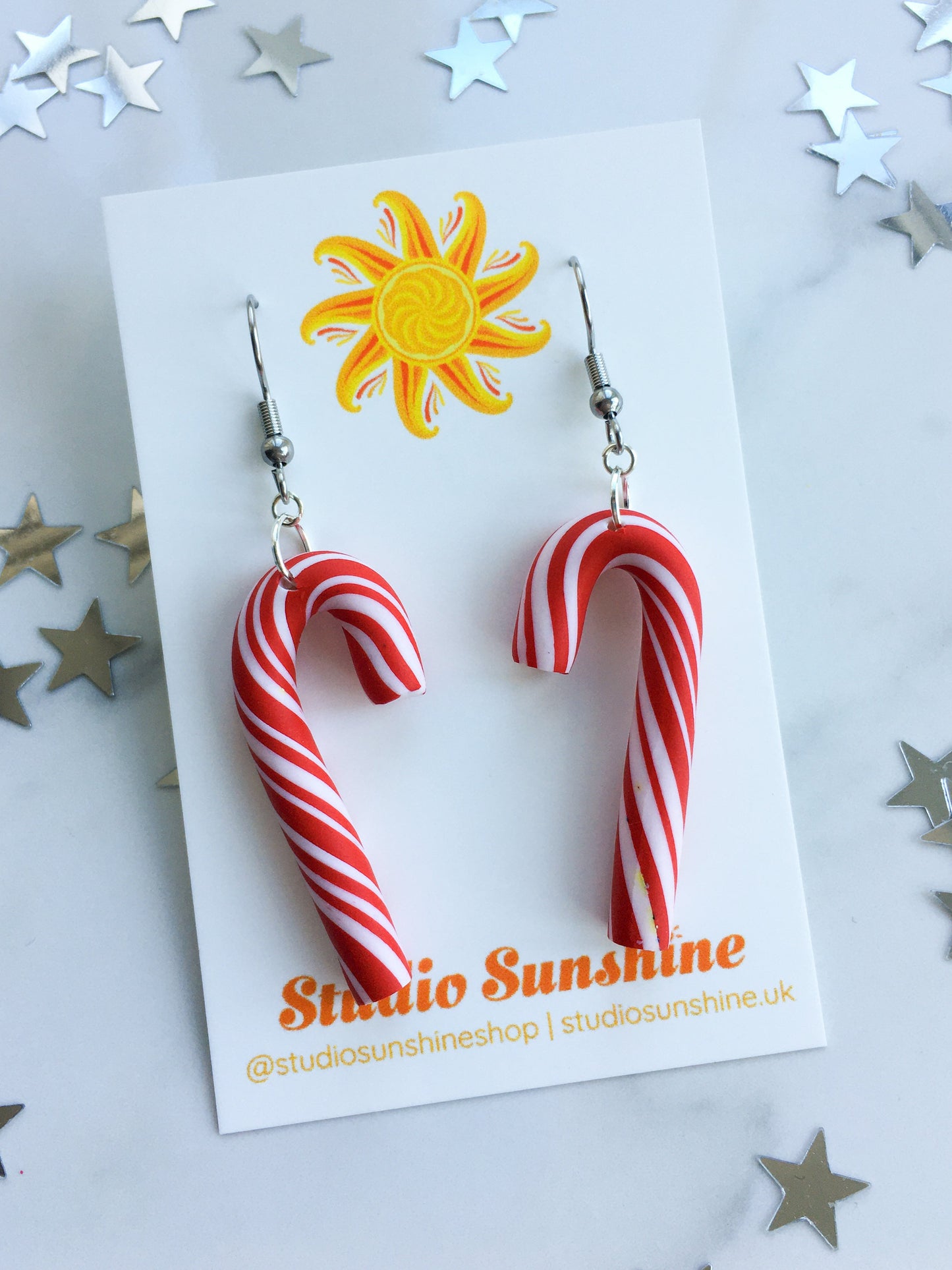 Candy cane-shaped earrings on a 'Studio Sunshine' branded card with star decorations.